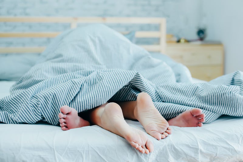 Feet of lovers couple lying on bed under blanket