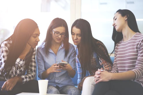Female friends dressed in casual wear choosing purchases in web store on smartphone talking to each ...