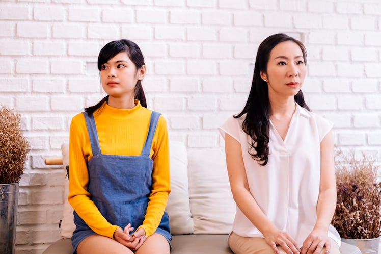 Unhappy mother and daughter in bad relationship sitting together and looking aside on brick wall bac...