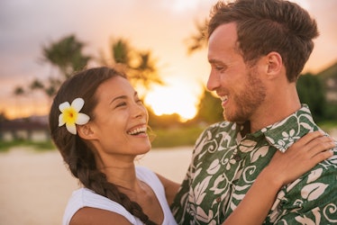 Happy couple lovers in love on romantic sunset beach vacation in Hawaii travel. Asian woman hugging ...