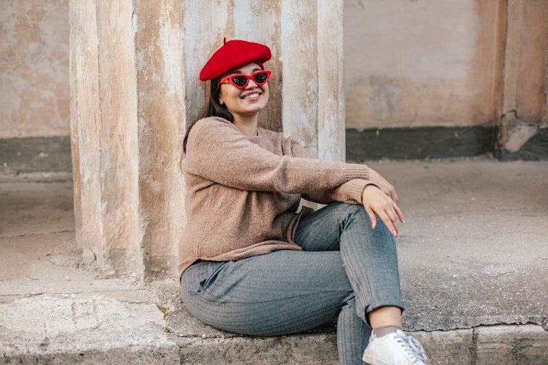 Plus size fashion model wearing simple sweater, red beret and chic sunglasses posing in the old city...