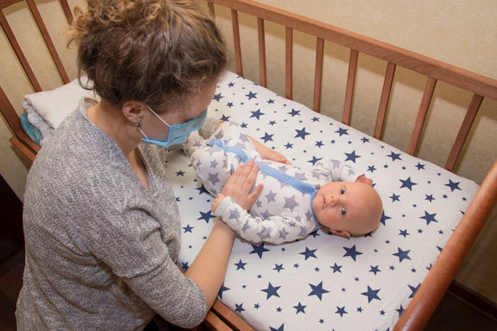 Mom wearing medical mask standing over baby in crib