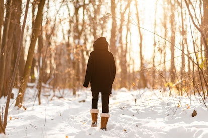 Winter snow walk woman walking away in snowy forest on woods trail outdoor lifestyle active people. ...