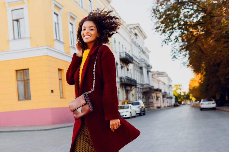 Smiling black girl in amazing winter outfit and accessories posing on street background. Wavy hair...