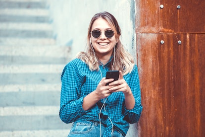 Portrait of a happy girl listening music on line with headphones from a smartphone in the street in ...