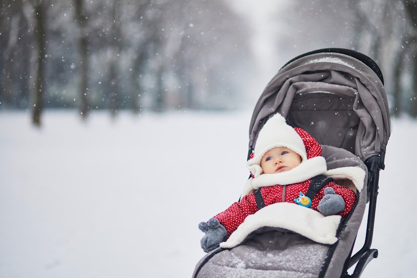 Happy smiling baby girl in stroller in Paris day with heavy snow. Little kid enjoying the very first...