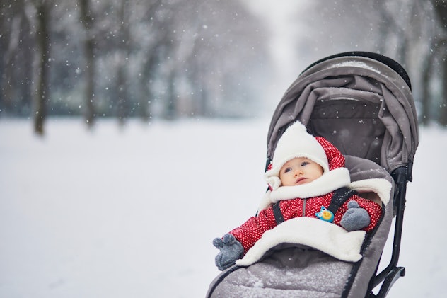 Happy smiling baby girl in stroller in Paris day with heavy snow. Little kid enjoying the very first...