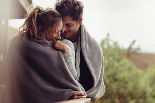 Romantic couple on a winter holiday. Man and woman standing together in a hotel room balcony wrapped...