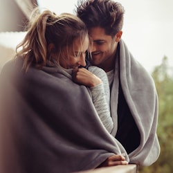 Romantic couple on a winter holiday. Man and woman standing together in a hotel room balcony wrapped...