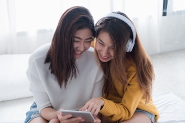 Two asia woman enjoy listening music app on tablet sitting on sofa in living room at home.Leisure di...
