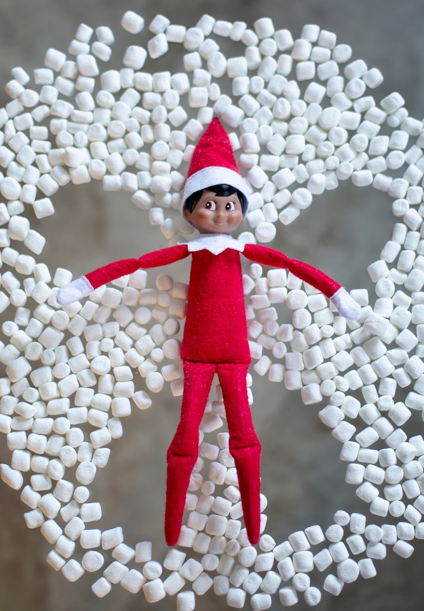 The elf on the shelf makes a snow angel from marshmallows. Elf in red suit and red hat