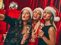 Happy New Year to you! Three beautiful sexy women in Santa hats with glasses of champagne take a sel...