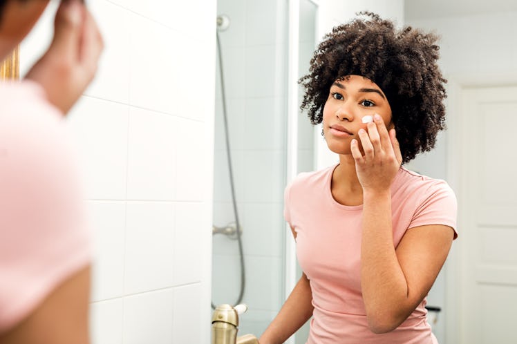 Young woman in bathroom looking in to the mirror and applying cream