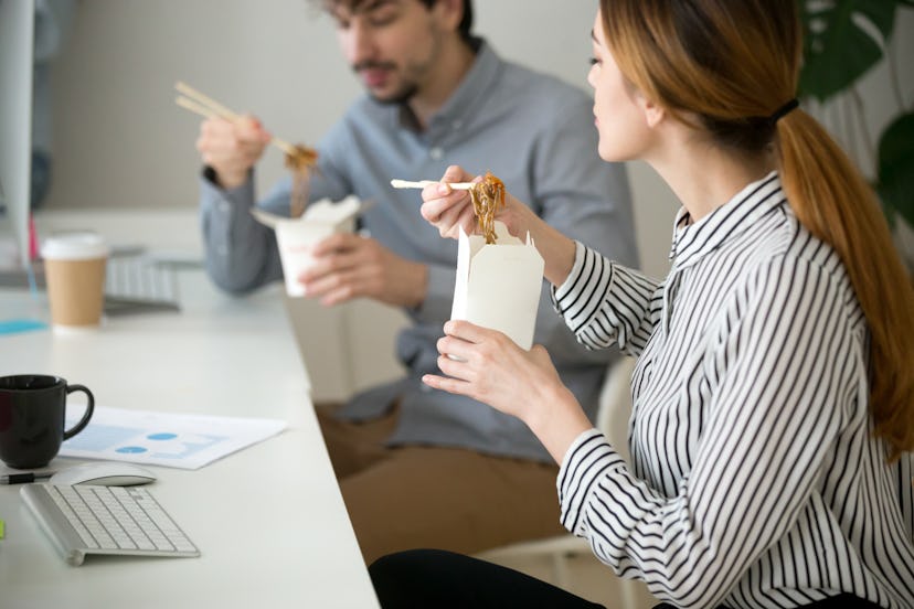 Office people eating chinese noodles holding boxes at lunch time, young woman and man employees enjo...