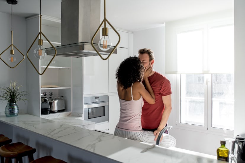 Affectionate interracial couple kissing while having healthy breakfast at home in the kitchen