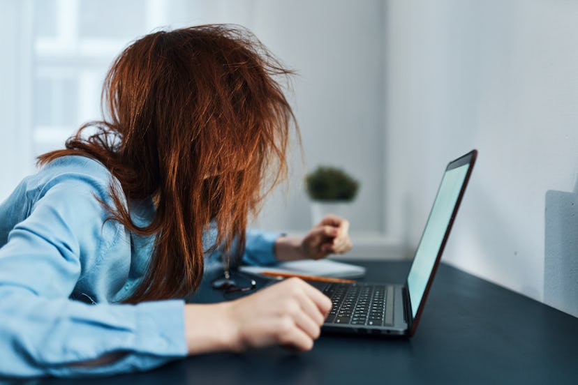 A woman with anxiety avoiding self care sits in front of her laptop with disheveled hair