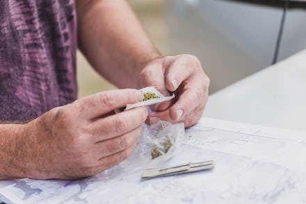 Close up of person's hands rolling a joint with marijuana (cannabis) and rice paper on top of a car ...