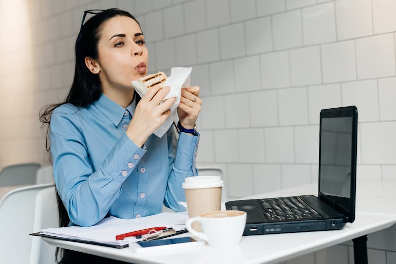 hungry business woman sitting in the office at the table and eating