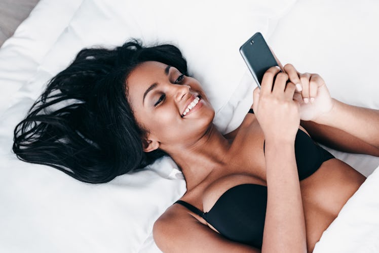 Great morning message. Top view of beautiful young African woman in black lingerie lying in bed and ...