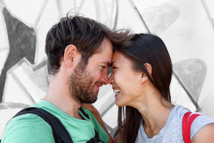 Interracial couple young happy Asian woman and Caucasian man lovers smiling laughing kissing portrai...