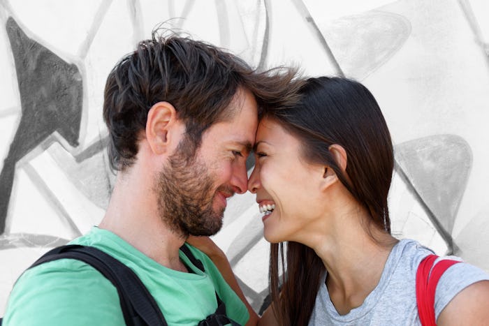 Interracial couple young happy Asian woman and Caucasian man lovers smiling laughing kissing portrai...