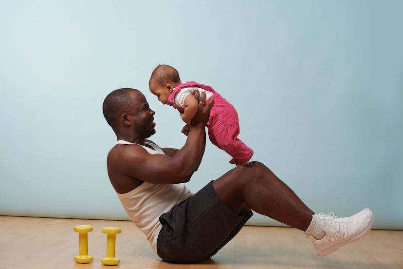 Handsome black young father is doing basic crunches while holding his tiny little baby daughter in h...