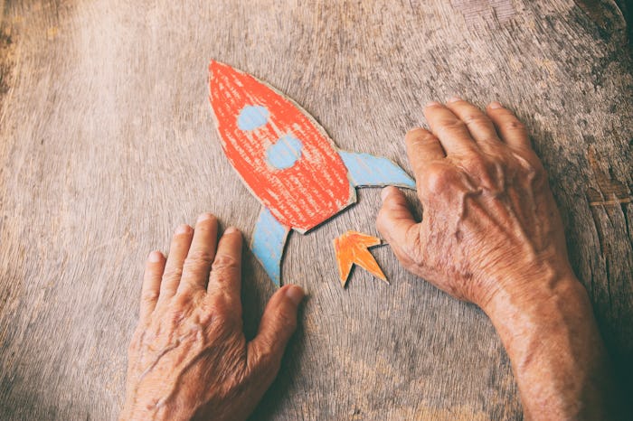 A close up of an elderly man holding a paper rocket on a wooden table. Concept of thinking about chi...