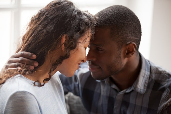 Close up of loving mixed race couple hug relaxing at home together looking in eyes, tender black man...