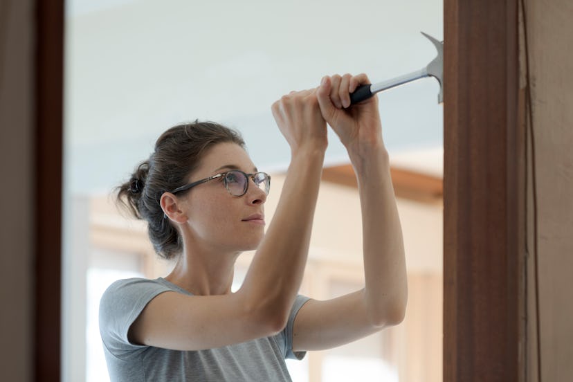 Woman repairing a door at home using a hammer: home renovation and DIY concept