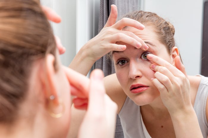 closeup of beautiful girl looking at herself leaning forward to bathroom mirror to apply or remove h...