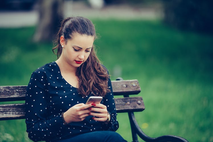 Girl texting on the smartphone sitting in a bench in a park - Image