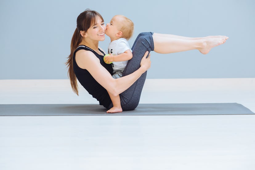 Mom swings a press and her sweet baby kissing her in cheek. A sports mother is engaged in fitness pi...