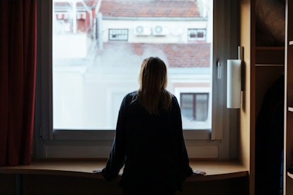 A woman with anxiety avoiding socializiation, standing and staring out the window