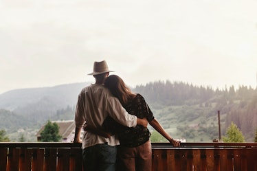 hipster couple hugging on porch of wooden house looking at mountains in evening sunset, romantic mom...