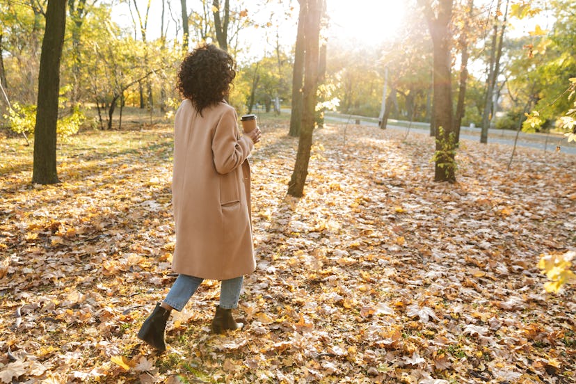 Back view photo of a beautiful young african woman walking outdoors in a spring park drinking coffee...