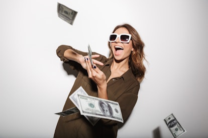 Portrait of a happy young woman in sunglasses throwing out money banknotes isolated over white backg...