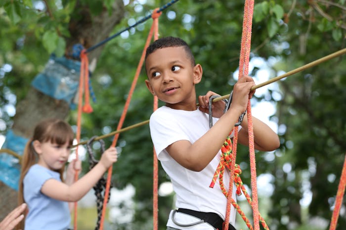 Little African-American boy climbing in adventure park. Summer camp