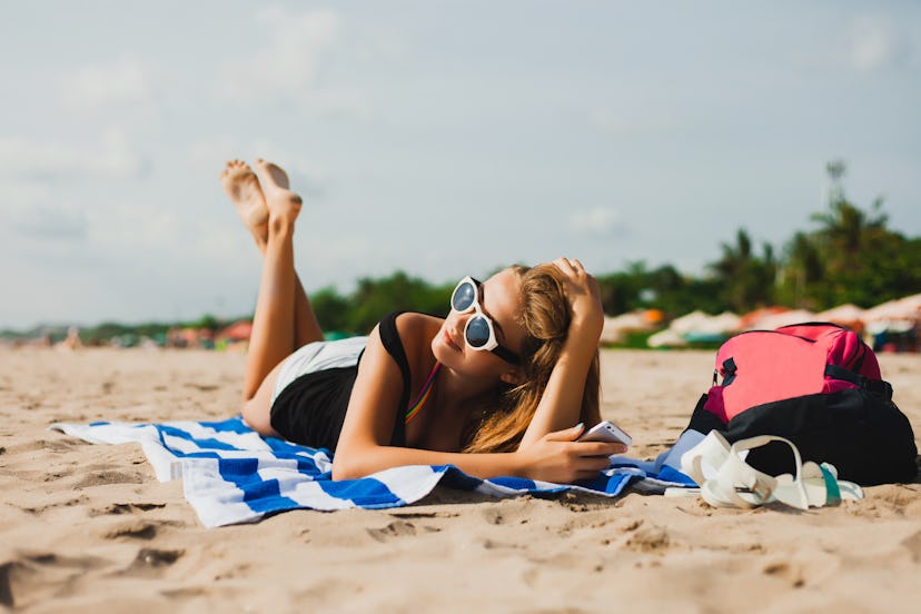 young beautiful girl lying on a towel on the beach with long hair with glasses talking on the phone,...