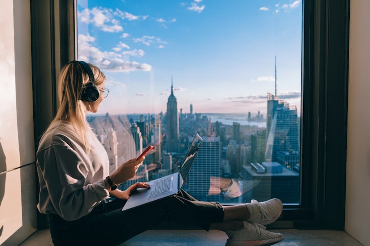 Blonde hair female blogger listening to music in headphones during freelance work on laptop computer...