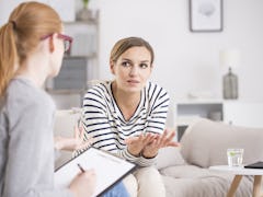 Red haired psychiatrist listening to her patient who experienced traumatic events, sitting on beige ...