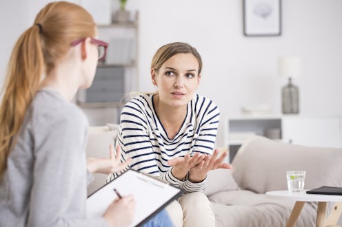 Red haired psychiatrist listening to her patient who experienced traumatic events, sitting on beige ...