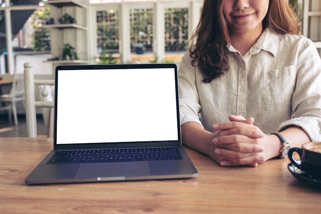 A woman presenting work with mockup laptop with blank white screen on wooden table