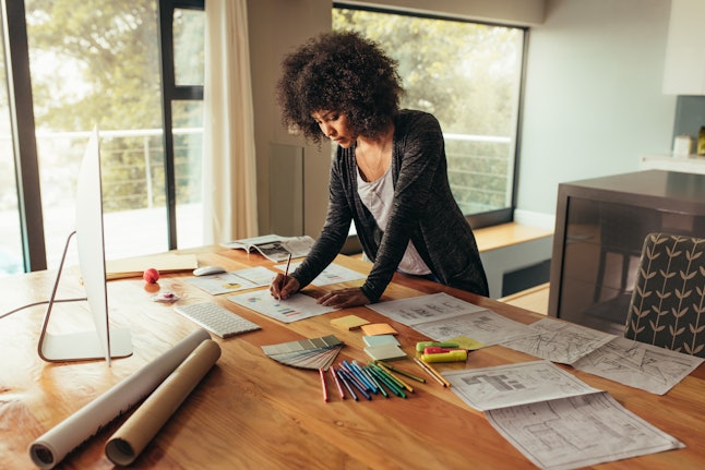 Young african businesswoman working on project. Woman working at home office, writing on a graph on a table.