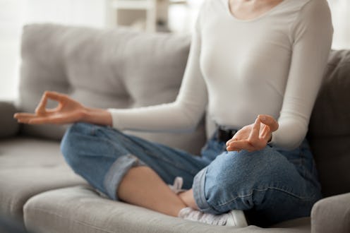 Close up of focused female sit on cozy couch meditating with mudra hands, calm woman practice yoga i...