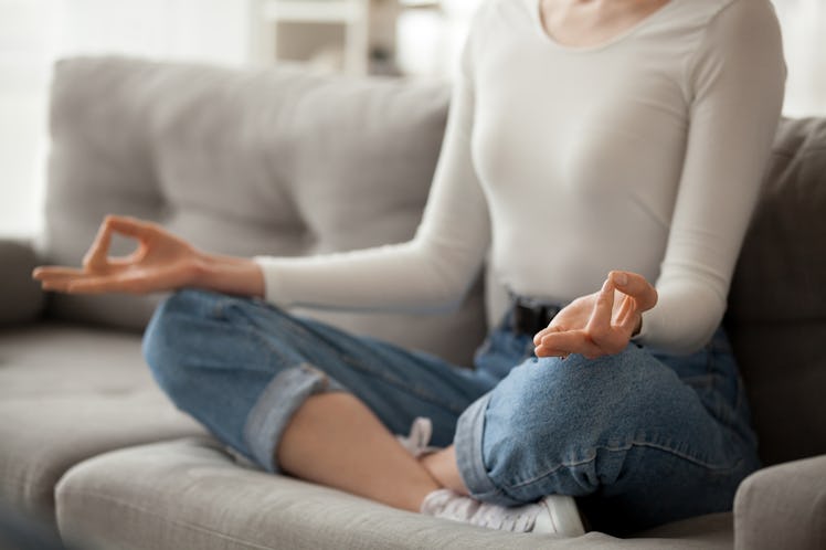 Close up of focused female sit on cozy couch meditating with mudra hands, calm woman practice yoga i...