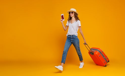 concept of travel. happy woman girl with suitcase and passport on yellow colored background