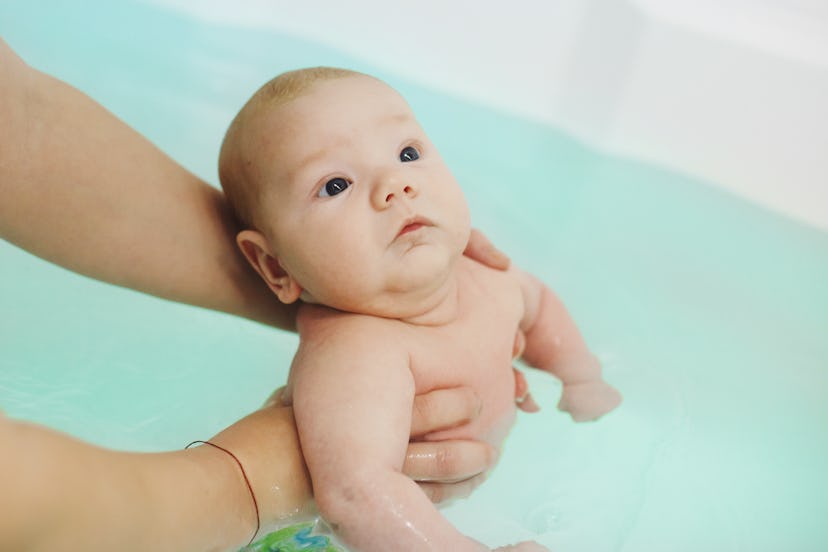 Mother's hands bathe their two-month-old baby in water. Children's health, hardening and active life...