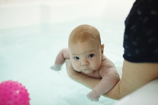 Mother's hands bathe their two-month-old baby in the water, the boy plays with a pink rubber ball. H...
