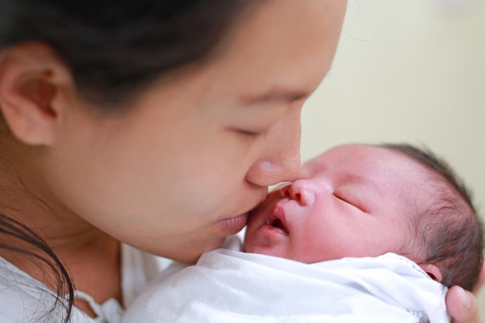 Mother kissing infant baby in her arms in hospital after delivery room.