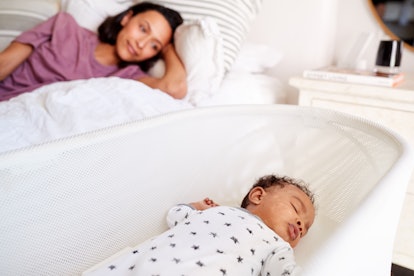 Close up of young African American adult mother lying on her bed looking down at her three month old...